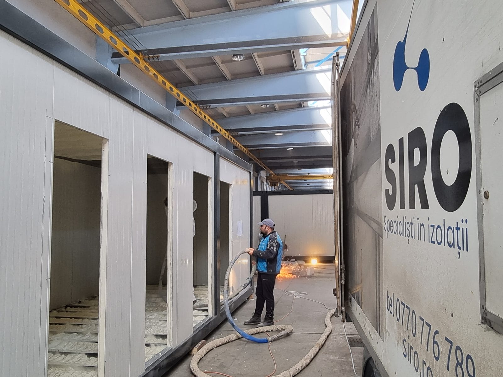 Hală industrială cu plafonul izolat, aplicatorul continuă lucrarea pe traveea următoare